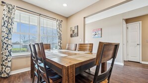 A dining area with a wooden table and chairs, a window with blinds, and a door. - Spin and Stay on Navajo (Bentonville)