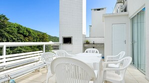 A terrace with a white table and chairs, a TV, and a stone shelf with plants. - Cobertura com Piscina na praia de Bombas (Bombinhas)