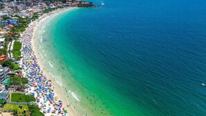A coastal cityscape with a wide beach lined with colorful umbrellas and a clear blue sea. - Cobertura com Piscina na praia de Bombas (Bombinhas)