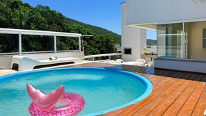 A swimming pool with a wooden deck, a white lounge chair, and a glass-enclosed room. - Cobertura com Piscina na praia de Bombas (Bombinhas)