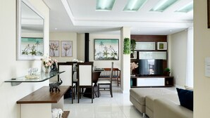 A modern living room with a sofa, a TV, a dining area with chairs and a table, and artwork on the walls. - Cobertura com Piscina na praia de Bombas (Bombinhas)
