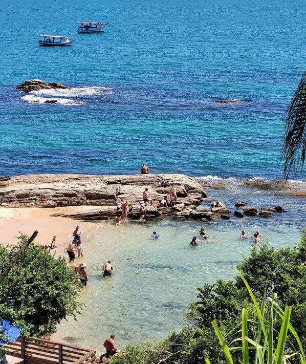 A coastal scene with clear waters, rocky formations, and people engaging in water activities. - Cobertura com Piscina na praia de Bombas (Bombinhas)