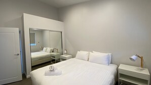 A hotel room with a large bed, a bedside table with a lamp, a mirror, and a wardrobe.