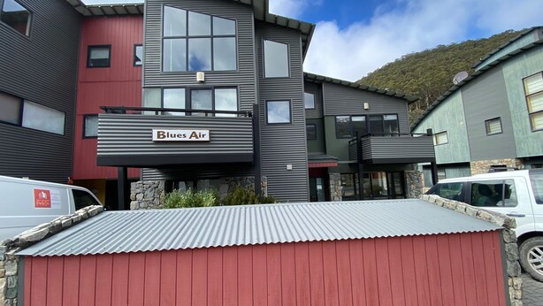 A multi-story building with a Blues Air sign, stone accents, and a corrugated metal roof.