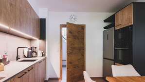 A modern kitchen with wooden cabinets, a built-in oven, and a dining area with a wooden table and bench. - Chalet Carina next ski slope (Zell am See)