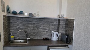 A compact kitchen with a built-in sink, a small refrigerator, a kettle, and a coffee maker on the countertop. - Sunset Paradise Oia (Santorini)