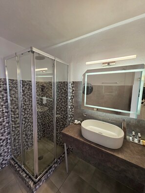 A modern bathroom with a glass-enclosed shower, a large sink, and a mirror above it.