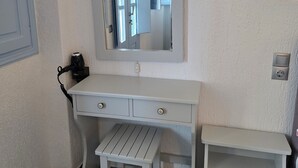 A white vanity with a mirror, a small stool, and a drawer unit. - Sunset Paradise Oia (Santorini)