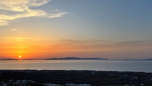 A coastal landscape with a sunset, distant mountains, and a view of the sea. - Sunset Paradise Oia (Santorini)