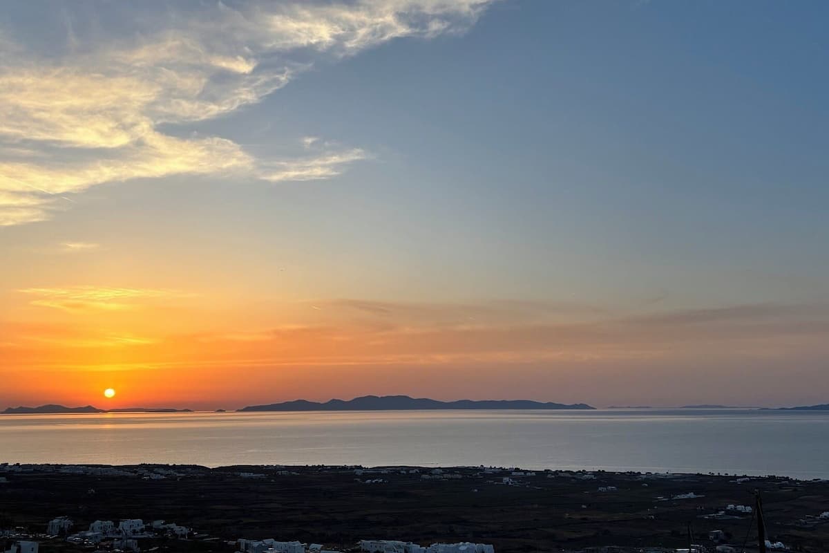 A coastal landscape with a sunset, distant mountains, and a view of the sea.