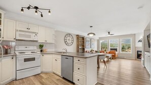 A modern kitchen with white cabinetry, a built-in oven, and a dishwasher. There is a dining area with a table and chairs, and a large window offering a view of the outdoors. - Satsuma | Close to Waterpark, Hot Springs & Golf (Fairmont Hot Springs)