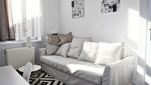 A modern living room with a white sofa, a round coffee table, and a patterned rug. There are two abstract art pieces on the wall and a window with sheer curtains. - Cracow Route #4 - Old Town (Kraków)