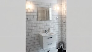 A modern bathroom with white subway tiles, a white sink with a mirror above it, and a small trash bin. - Cracow Route #4 - Old Town (Kraków)
