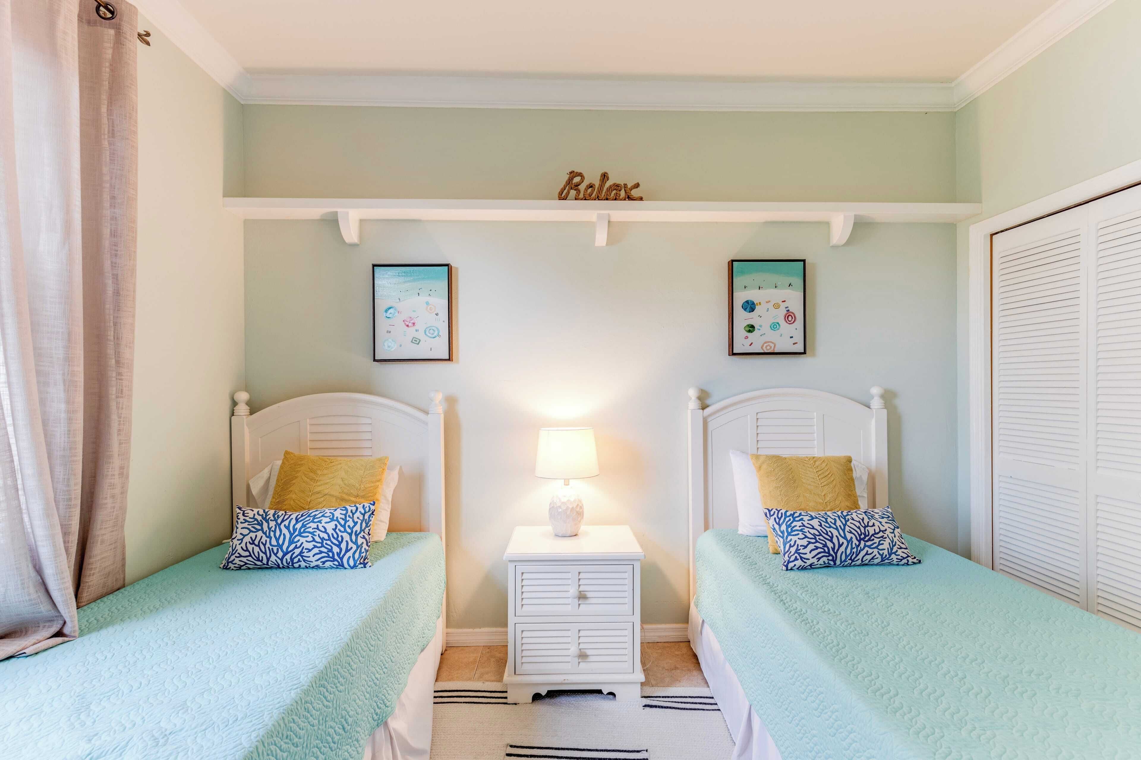 Une chambre avec deux lits, une table de chevet avec une lampe et une étagère sur laquelle est posé un panneau indiquant « Détendez-vous ».