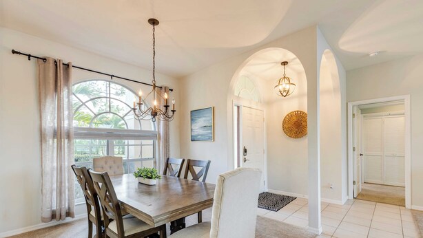 A dining area with a wooden table, chairs, and a chandelier. There is a window with curtains, a door, and a rug on the floor. - Private Pool, Pond Views, & Bonus Lounge in Gated Naples Community Drive to Dining & Sand (Naples)
