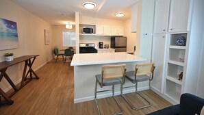 A modern kitchen with white cabinetry, a central island with bar stools, a microwave, and a refrigerator. - The Austin Vacation (Austin)