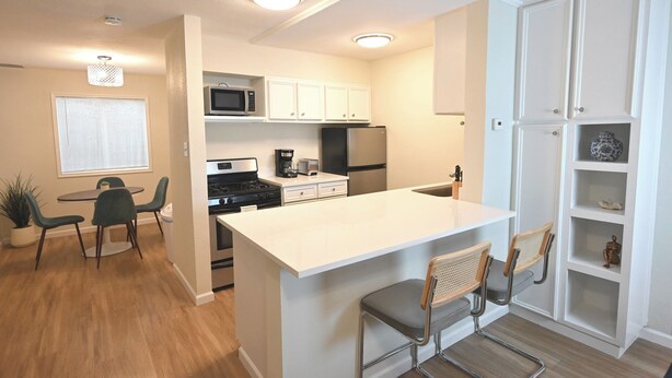 A modern kitchen with white cabinetry, a central island with bar stools, a microwave, stove, and refrigerator. - The Austin Vacation (Austin)