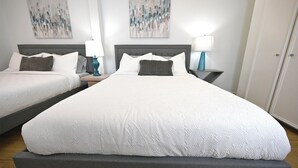 A hotel room with two beds, a grey headboard, white bedding, and abstract wall art. - The Austin Vacation (Austin)