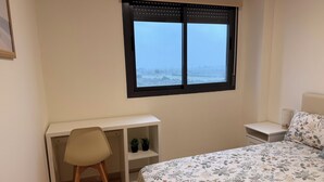 Ein Schlafzimmer mit Bett, Schreibtisch, Stuhl, Nachttisch und einem Fenster mit Blick auf eine verschneite Landschaft.