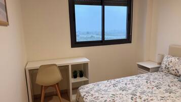 Een slaapkamer met een bed, een bureau, een stoel, een nachtkastje en een raam met uitzicht op een besneeerd landschap.