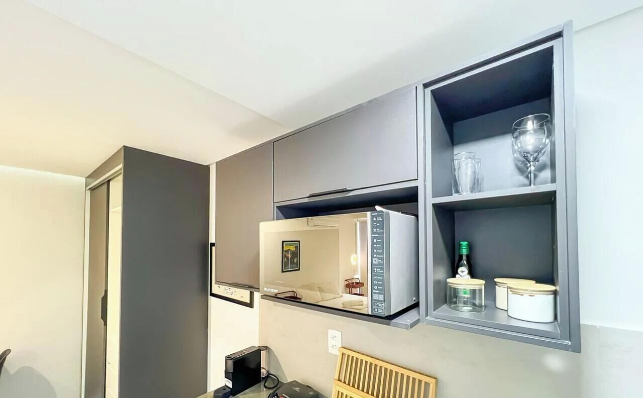 A modern kitchen with a built-in microwave, a small table with a chair, and a shelf with glassware and jars.