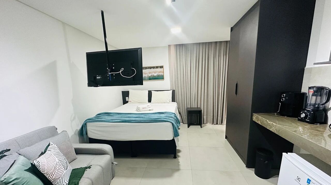 A modern hotel room with a bed, a sofa, a TV, a coffee maker, and a small table.