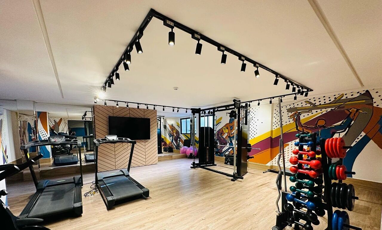 Ein Fitnessraum mit Laufbändern, einer Gewichtbank und einer Wand mit farbenfroher Kunst.