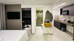 Hotelkamer met een bed, een aan de muur bevestigde televisie, een badkamer met douche en een kitchenette met magnetron en koffiezetapparaat.