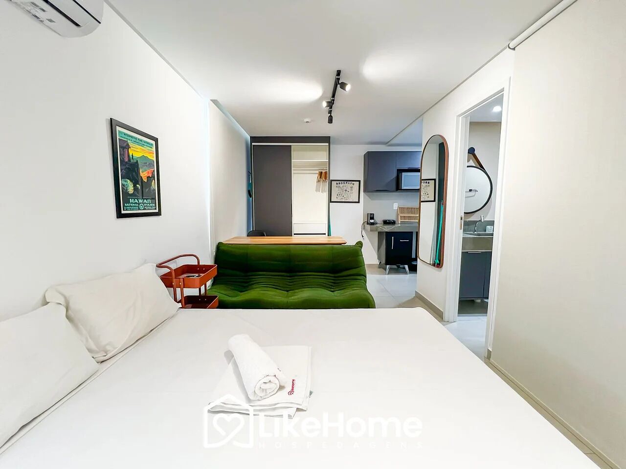 Una habitación de hotel con una cama, un sofá verde, una mesita y un televisor montado en la pared.
