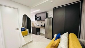 Een moderne woonkamer met een bank, een grote spiegel en een keuken met een koelkast en magnetron.
