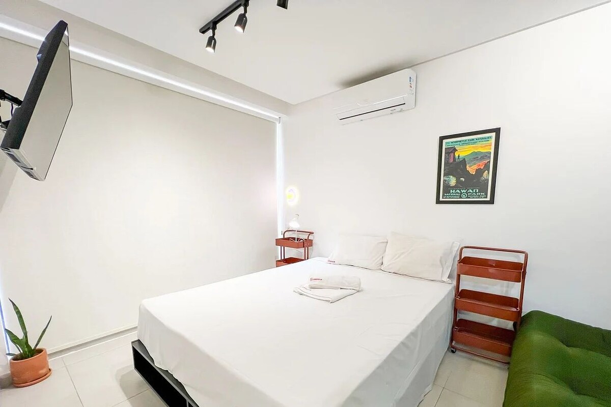 Una habitación de hotel moderna con una cama grande, una mesita de noche pequeña, un sofá verde y un aire acondicionado instalado en la pared.