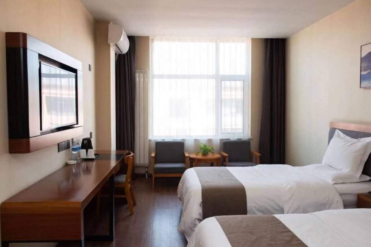 A hotel room with two beds, a desk, a TV, and a window with curtains.