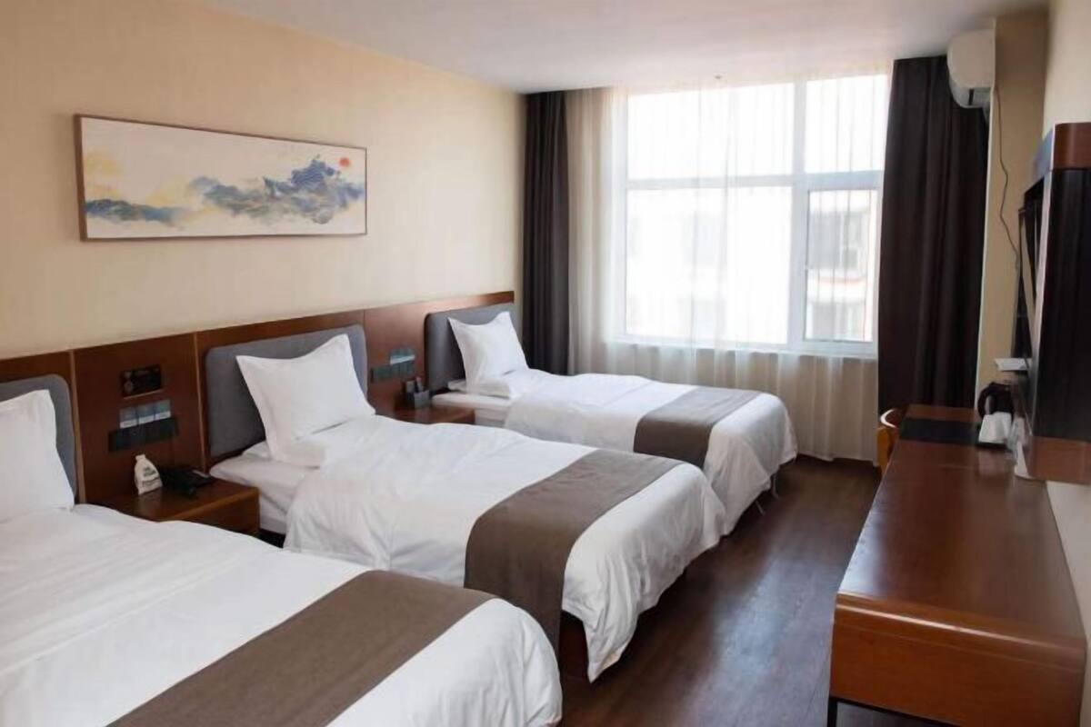 A hotel room with two beds, a wooden desk, a TV, and a window with curtains.
