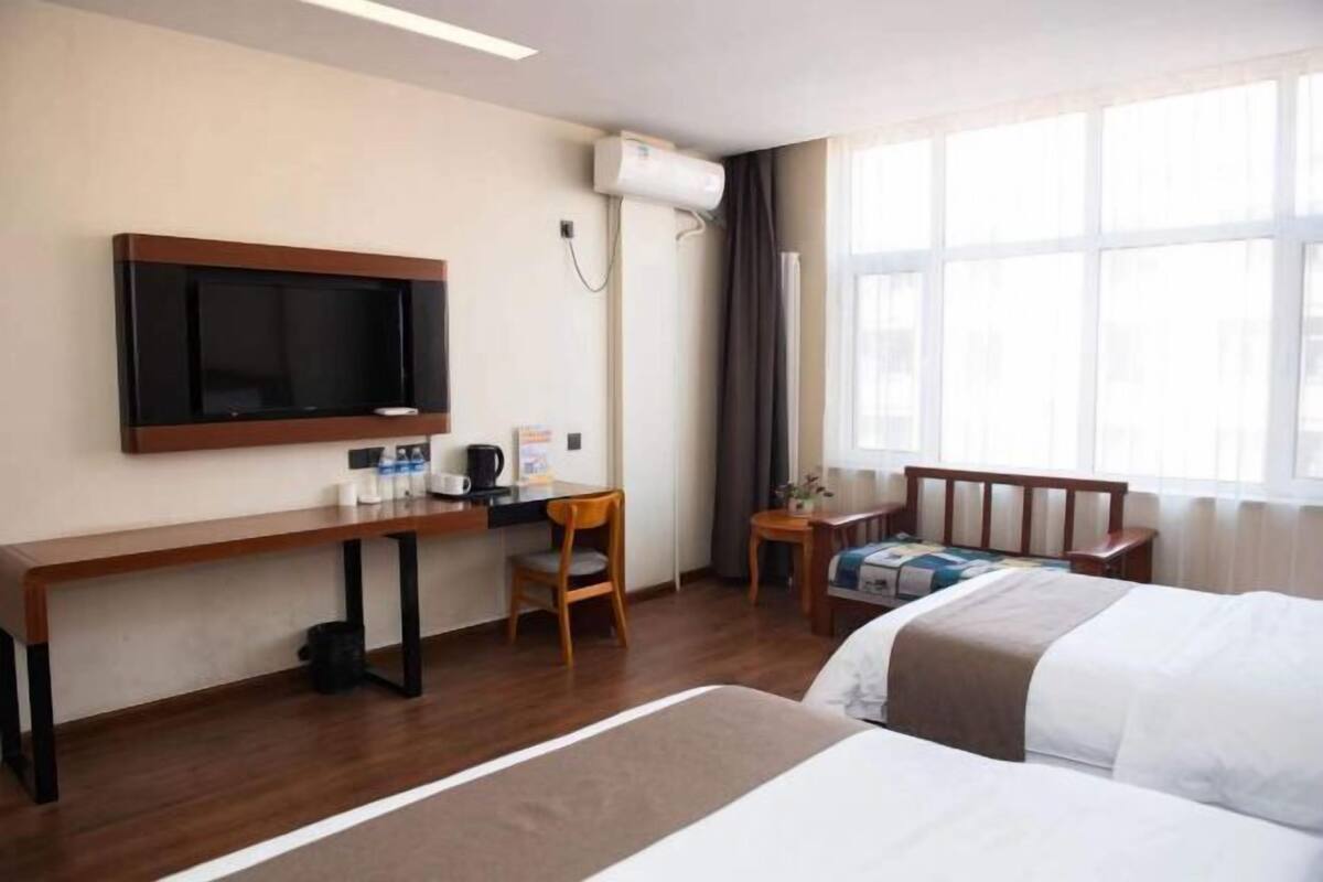 A hotel room with a bed, a desk with a chair, a television, and a window with curtains.