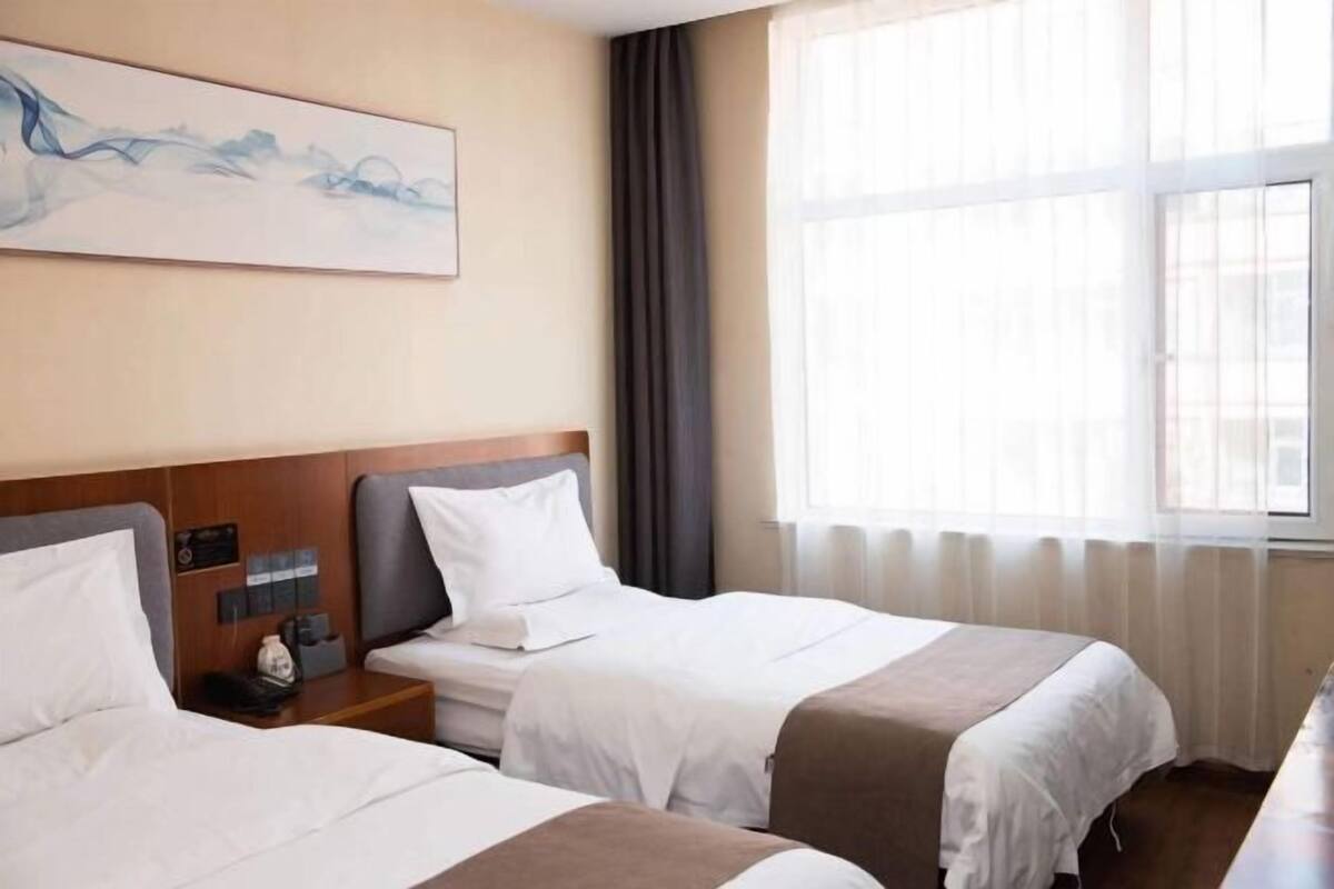 A hotel room with two beds, a large window with curtains, a painting on the wall, and a nightstand with a phone.