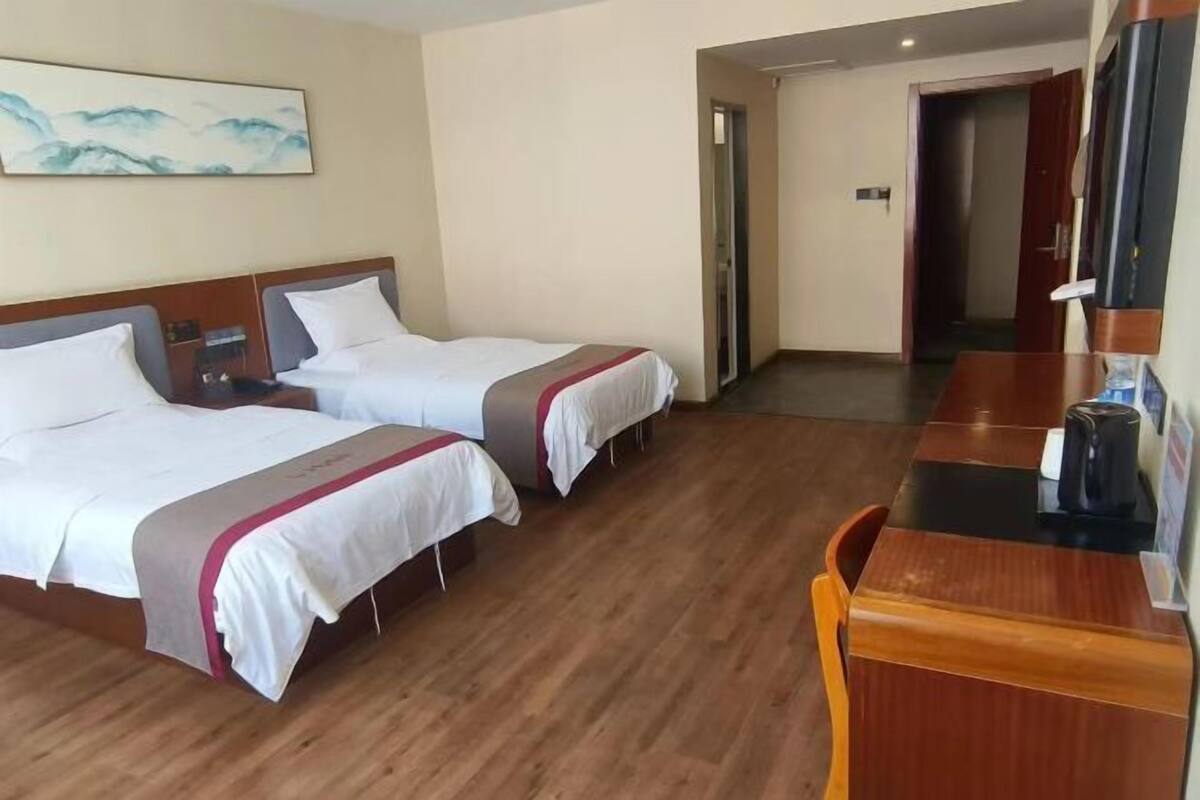 A hotel room with two beds, a wooden desk, a television, and a painting on the wall.