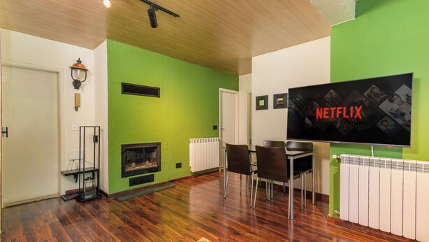 A living room with a green wall, a fireplace, a dining area with chairs, and a flat-screen TV mounted on the wall. - Warm Getaway 24/7 Power in Kfardebian (Jabal Lubnan)