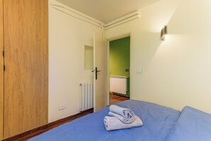 A bedroom with a bed, a rolled towel, a radiator, and a door leading to another room. - Warm Getaway 24/7 Power in Kfardebian (Jabal Lubnan)