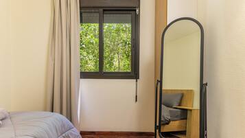 Un dormitorio con cama, ventana con cortinas, espejo y vistas a zonas verdes.