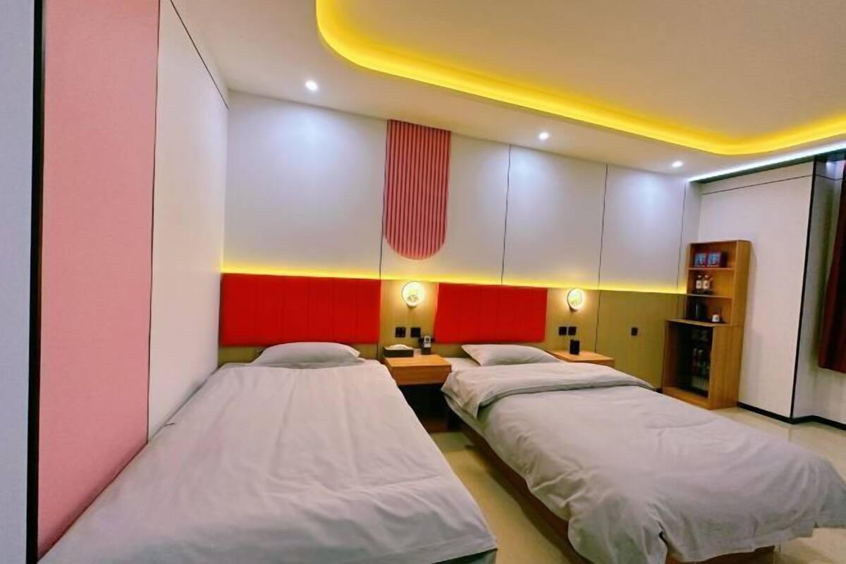 Habitación de hotel con dos camas individuales, una pared de acento roja, una mesita de noche de madera, una estantería y una cortina roja.