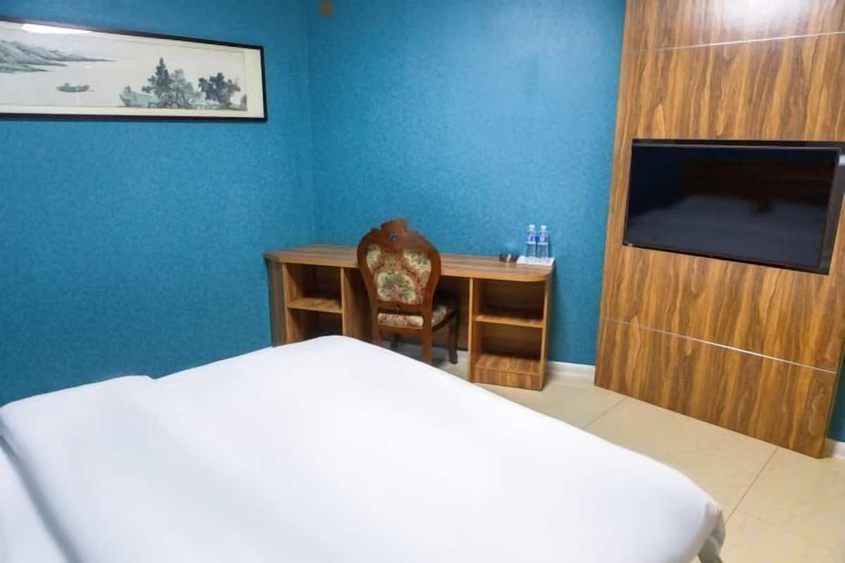 Habitación de hotel con cama, escritorio y silla, televisor y un cuadro en la pared.