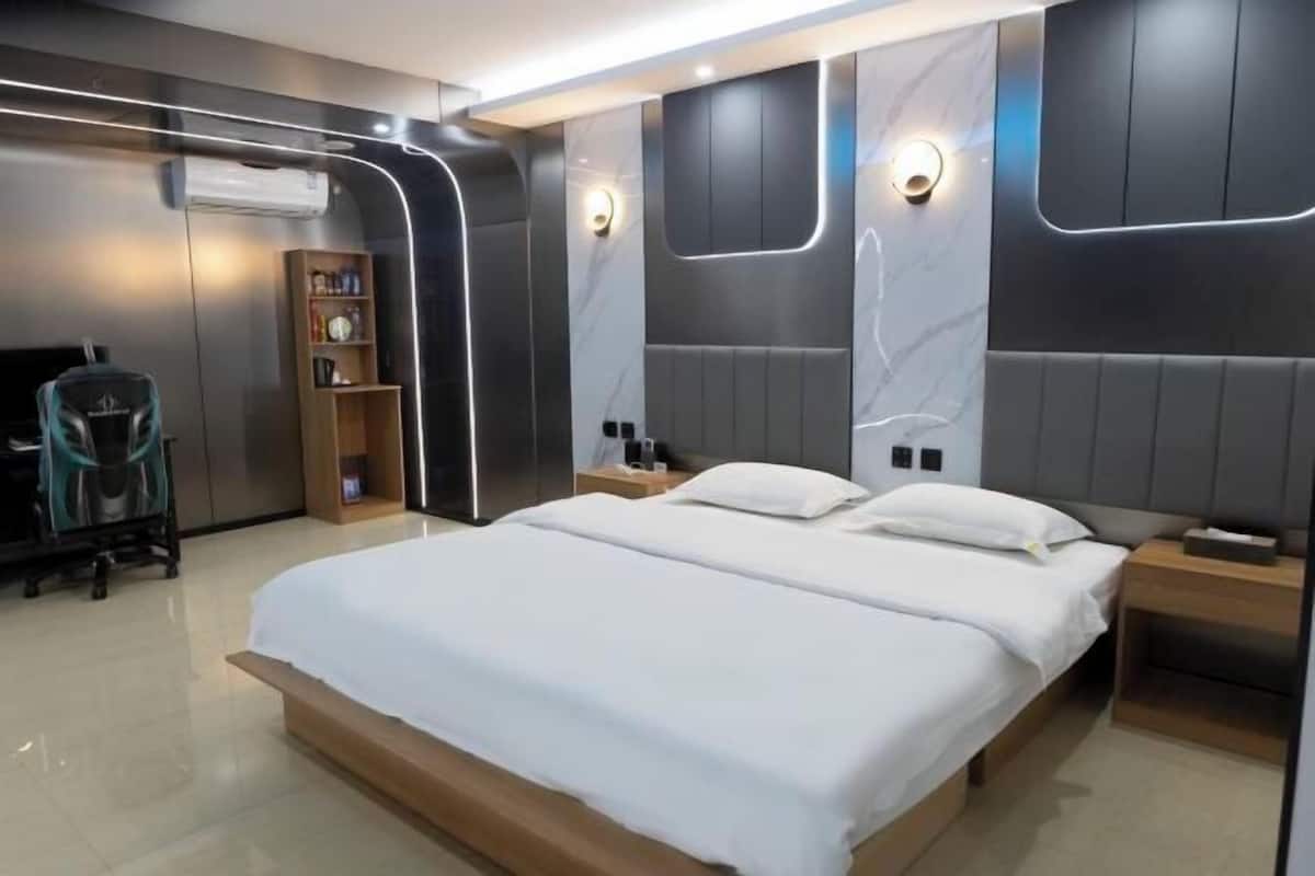 Una habitación de hotel moderna con una cama grande, mesitas de noche, una estantería y un escritorio.