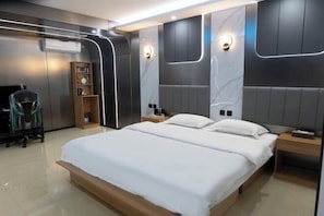 Una habitación de hotel moderna con una cama grande, mesitas de noche, una estantería y un escritorio.