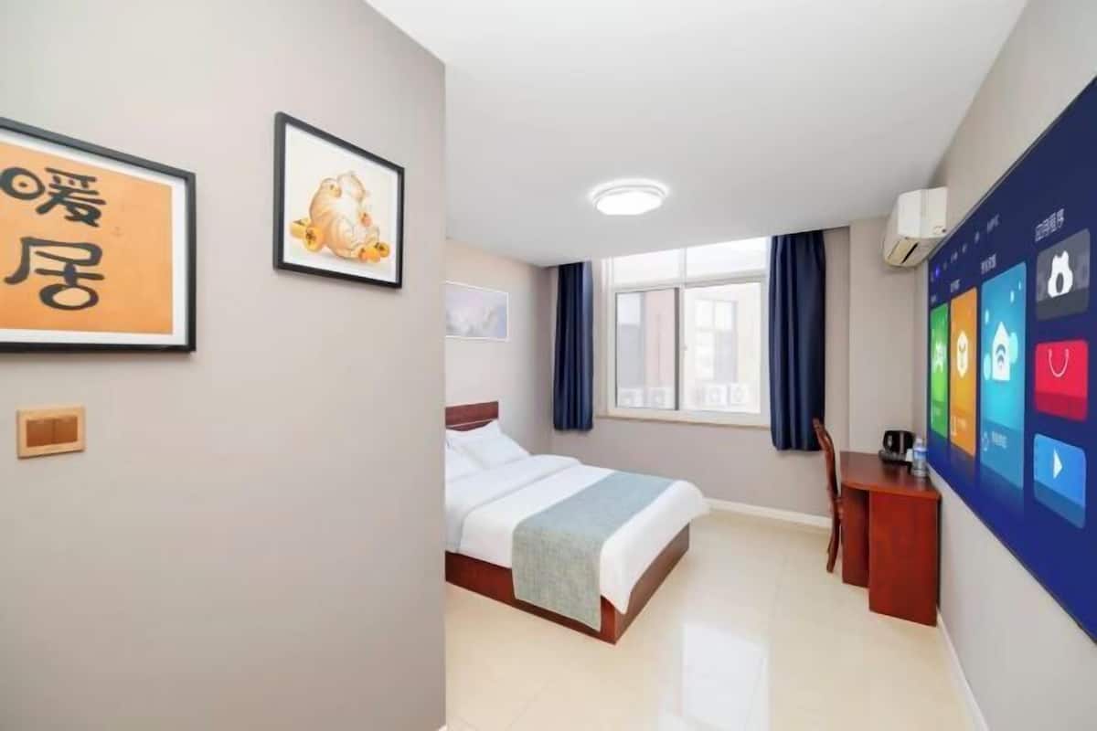 Habitación de hotel con cama, escritorio, aire acondicionado de pared y una pantalla digital que muestra iconos.