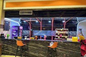 Zona de bar con mostrador de mármol, dos taburetes naranjas e iluminación de neón en el techo.