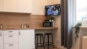 A modern kitchen with white cabinets, a black microwave, two black stools, and a TV mounted above the counter. - Cracow Vistula Boulevard #1 - Old Town (Kraków)