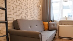 A modern living room with a grey sofa, a small white side table, and a brick-patterned wall. - Cracow Vistula Boulevard #1 - Old Town (Kraków)