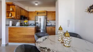 A modern kitchen with wooden cabinets, a stainless steel refrigerator, and a marble dining table with two chairs.