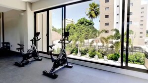 A gym with two stationary bikes and a large window with a view of buildings and greenery.