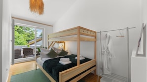 Un dormitorio con una cama litera de madera, un tapete verde, una bata blanca y vistas al exterior.
